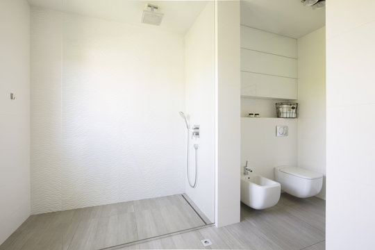 Glass shower and toilet in white spacious bathroom interior. Real photo