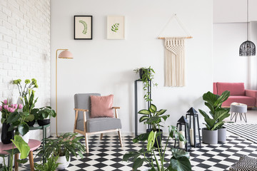 White, brick wall and pink pillow on an armchair with houndstooth pattern in open space living room interior with lots of plants. Real photo