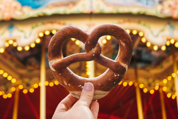The girl is holding a traditional German pretzel. Carousel or merry-go-round and celebration in the...