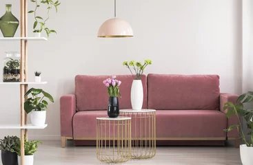 Poster Real photo of a feminine living room interior with gold and marble tables with fresh flowers standing in front of a cozy pink sofa © Photographee.eu