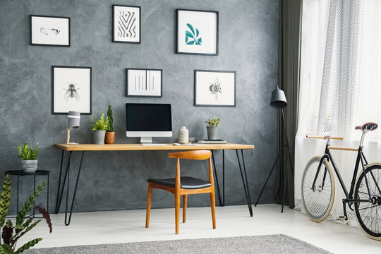 Bicycle in a grey home office interior with a wooden desk and chair, graphic collection and computer with an empty screen. Place your product