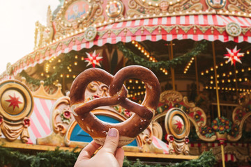 The girl is holding a traditional German pretzel. Carousel or merry-go-round and celebration in the...