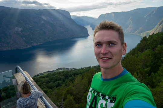 Young traveller taking selfie on the top with Beautiful fjord on background in Norway