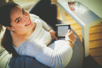 Fototapeta na wymiar Smiling young woman sitting on sofa with touchpad