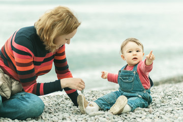 Cute baby and his mother playing with pebbles on beach