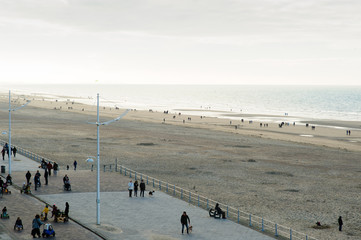 people strolling on the sea-wall at the North Sea at fall, other are playing with there childeren on the beach