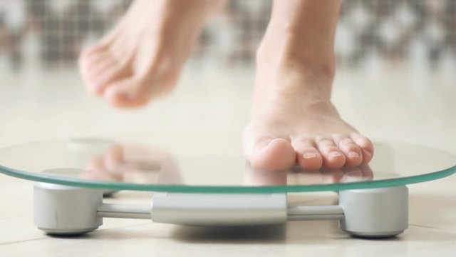 Woman feet standing on electronic scales for weight control  on the bathroom.   Close-up .