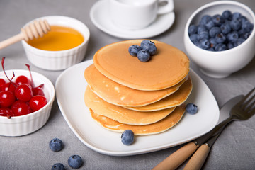 Pancakes with blueberries, cherries and honey. Close-up. Selective focus.