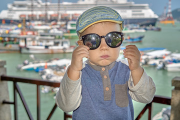 Cute boy in the sunglasses posing with cruise ship in background