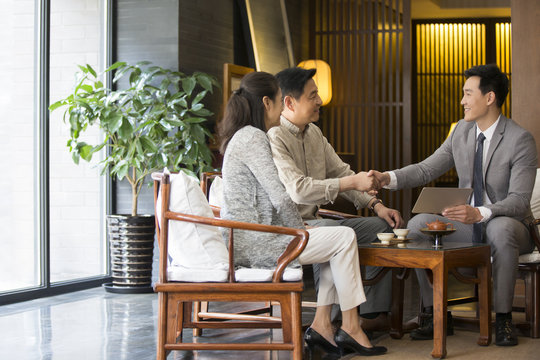 Confident financial consultant shaking hands with mature couple