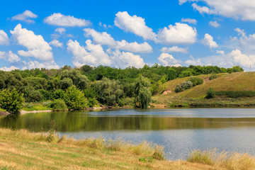 Obraz premium Summer landscape with beautiful lake, green meadows, hills, trees and blue sky