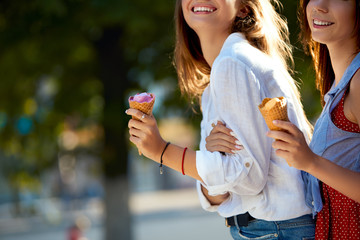 Naklejka premium Close up shot of ice cream cones in hand of a woman standing with her friend. Two young women outdoors eating icecream on a sunny day. Isolated view, no face, copyspace for designers. Summer theme.