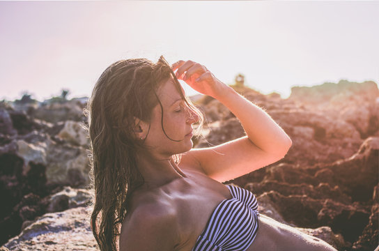 A woman touches her wet hair with her hand, sunbathing under the bright sun