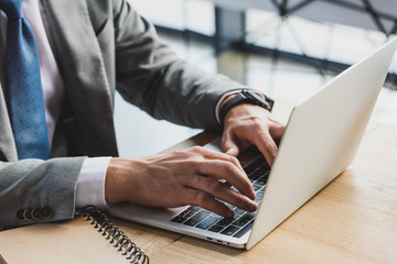 close-up partial view of businessman typing on laptop at workplace