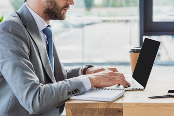 cropped shot of businessman in suit using laptop with blank screen in office