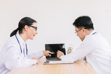 Two doctors are discussing the results of a patient's presentation of the results of a tablet computer sitting at a desk.