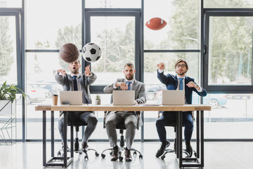 young office workers throwing balls while working with laptops in office