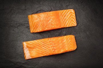 Two slices of salmon with on a black background with copy space, overhead photo