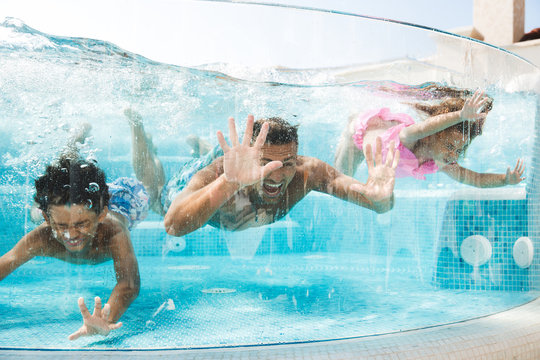 Photo of adult man with children diving and swimming under water in transparent pool, during summer vacation