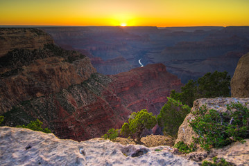 Grand Canyon rocky desert with Colorado River and sunset background. South Rim colorful mountainous landscape view in warm color shades of yellow, orange, dark burgundy reds and brown