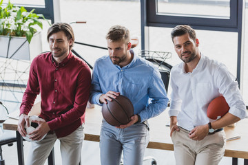 high angle view of young businessmen holding basketball, soccer and rugby balls in office