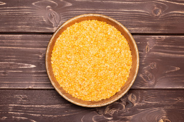 Lot of whole raw red lentils with wooden bowl flatlay on brown wood