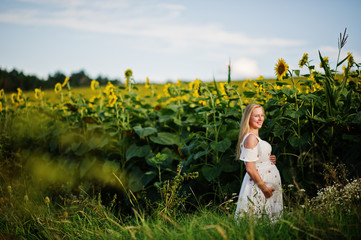 Blonde pregnant mother in sunflowers field. Happy moments of pregnancy.