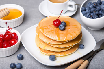 Pancakes with blueberries, cherries and honey. Close-up. Selective focus.