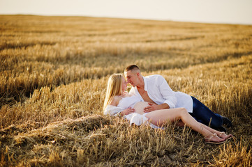 Naklejka na ściany i meble Pregnant couple in wreath field at white underwear clothes on sunset. Happy moments of pregnancy.
