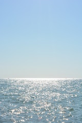 Beautiful border between the blue sky and the black sea with small waves and fine golden and bright reflections of the sun on the water