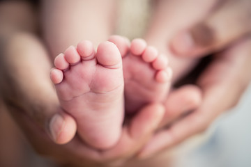 Feet of a newborn baby in the hands of parents. Happy Family oncept. Mum and Dad hug their baby's...