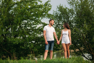 Naklejka na ściany i meble Dating in park. Love couple standing together on grass near the lake. Romance and love
