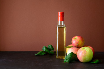Apple vinegar in glass bottle and fresh apples on brown wooden desk
