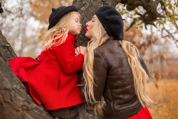 Fototapeta premium girl in a red coat climbed up an old tree and her mother supports