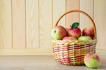 Wooden basket with red and green apples on front of brown wooden wall. Harvest concept