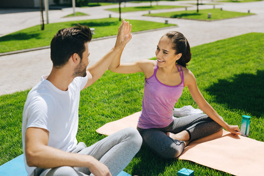 Great mood. Cheerful positive couple giving high five to each other while sitting on yoga mats