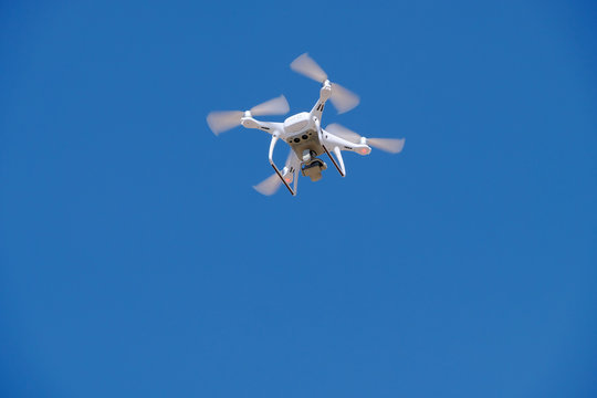 White drone for photography flies in the blue sky