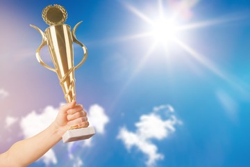 Hand holding golden trophy on sky background