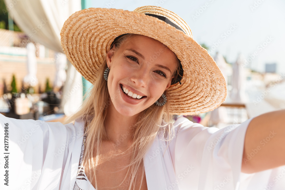 Sticker photo closeup of beautiful young woman 20s in straw hat and swimwear taking selfie, while sunbathing