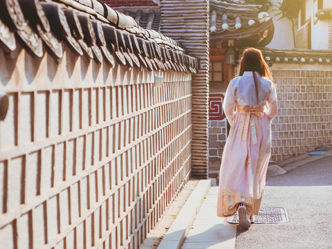 travel and tourist korea concept from backside long hair woman in korea traditional cloth (hanbok) walk in vintage town and old brick wall with soft focus background