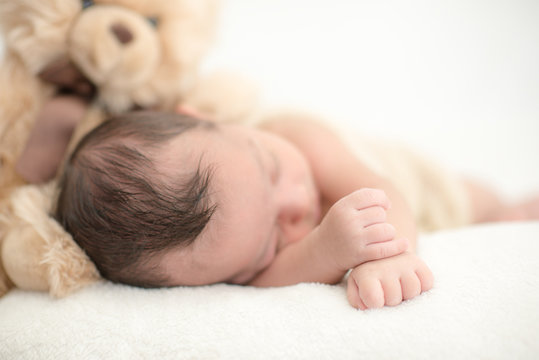 Cute newborn baby sleeps on a blanket with a toy teddy bear - happy family moments