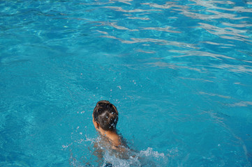 Teenager wet hair from behind sitting in swimming pool alone blue water