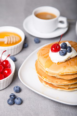 Pancakes with blueberries, cherries, sour cream, honey and coffee. Close-up. Selective focus.