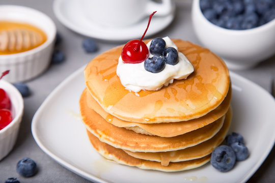 Pancakes with blueberries, cherries, sour cream, honey and coffee. Close-up. Selective focus.