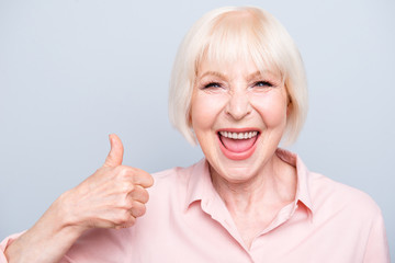 Old excited lady showing thumbs up gesture, laughing on grey bac