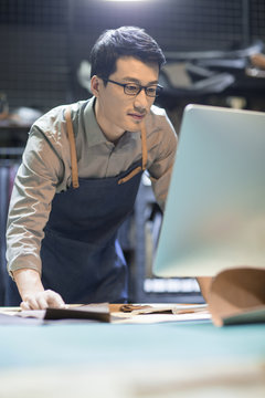 Young leather craftsman using computer in studio 