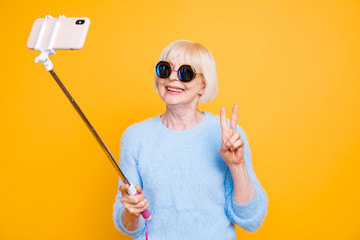 Portrait of modern grandmother holding and using selfie stick wi
