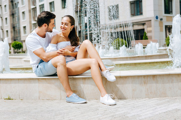 Romantic feelings. Pleasant nice man hugging his girlfriend while sitting together with her near the fountain