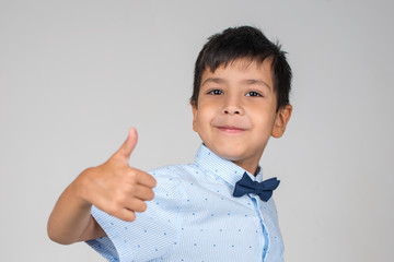 Portrait of smiling boy wearing; blue shirt with tie-bow showing gesture OK on a gray background in the studio