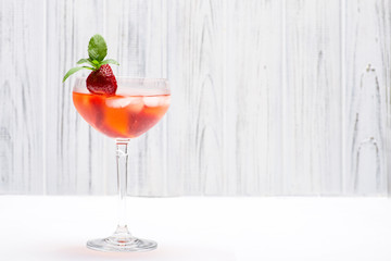 The glass with the soft strawberry drink decorated with strawberry and leaves of mint costs at a wooden white wall